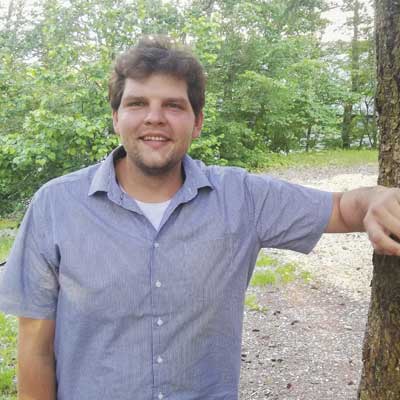 Auf dem Bild ist das Vorstandsmitglied Dimitri Wedmann zu sehen. Er ist an einem Baum angelehnt und lacht n die Kamera.