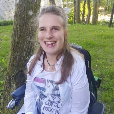 Auf dem Bild ist das Vorstandsmitglied Lea Voitel zu sehen. Sie sitzt im Rollstuhl und lacht in die Kamera