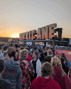 Man sieht eine große Menschenmenge und eine große Skulptur die in Form von Buchstaben das Wort "Hurricane" abbildet. Im Hintergrund geht die Sonne gerade unter.